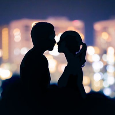 A man and woman in silhoette facing each other with coloured lights behind 